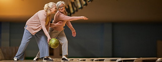 Image of senior woman showing another senior woman how to bowl